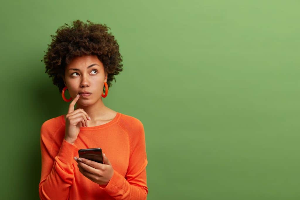 Woman, wearing an orange jumper, holding her phone while looking confused about legalisation.