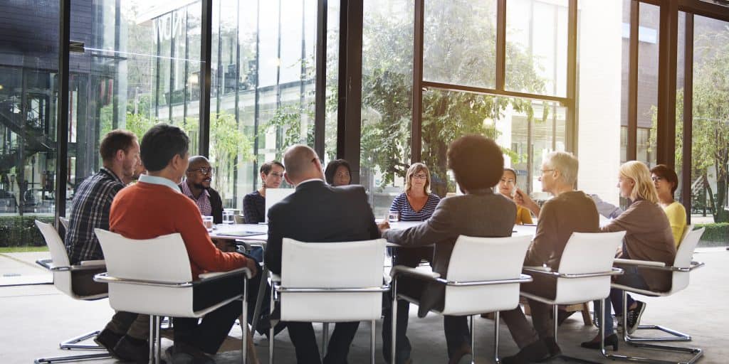 A diverse group of workers sat around a table discussing jobs overseas. Some are wearing suits, others more casual.
