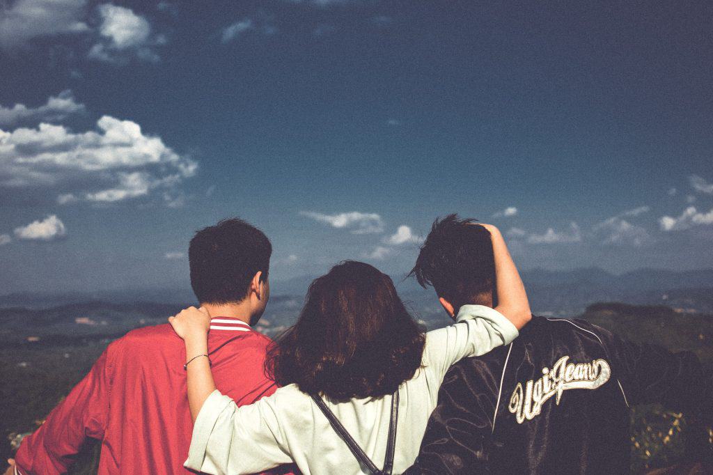 Three friends with their arms around each other - a girl and two boys, looking out over the landscape for teaching English in China