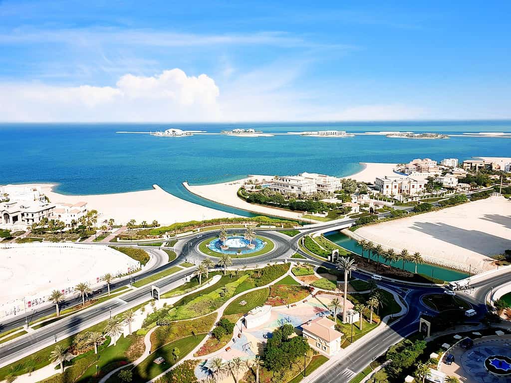 A picturesque photo of Qatar - a roundabout and green park is in the foreground, and a clear blue sea is in the background