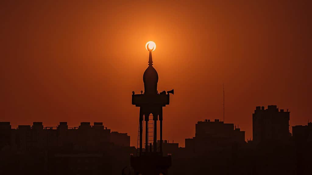 A silhouette of a tower, with a crescent moon on the top, against a setting sun. The silhouette of the moon sits inside the sun. For Kuwait legalisation blog.