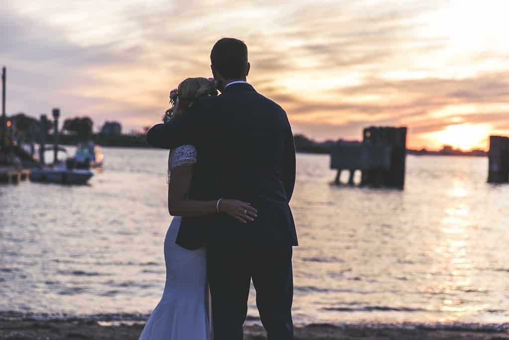 A couple embracing, looking out at the sunset across the harbour.