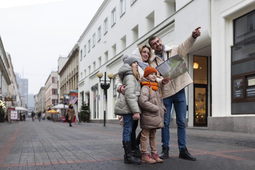 A family in a new city, after moving internationally, getting their barings. There are a mum, dad and two young girls. They are wearing winter coats and the children have woolly hats.