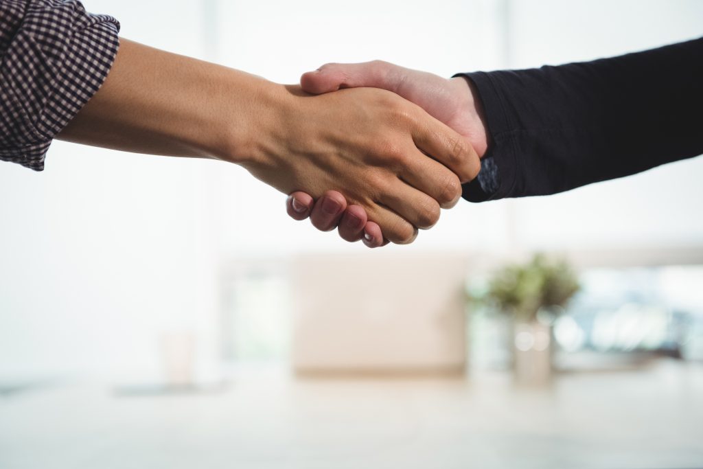 Two business people, a man and a woman, shaking hands in a business environment.
