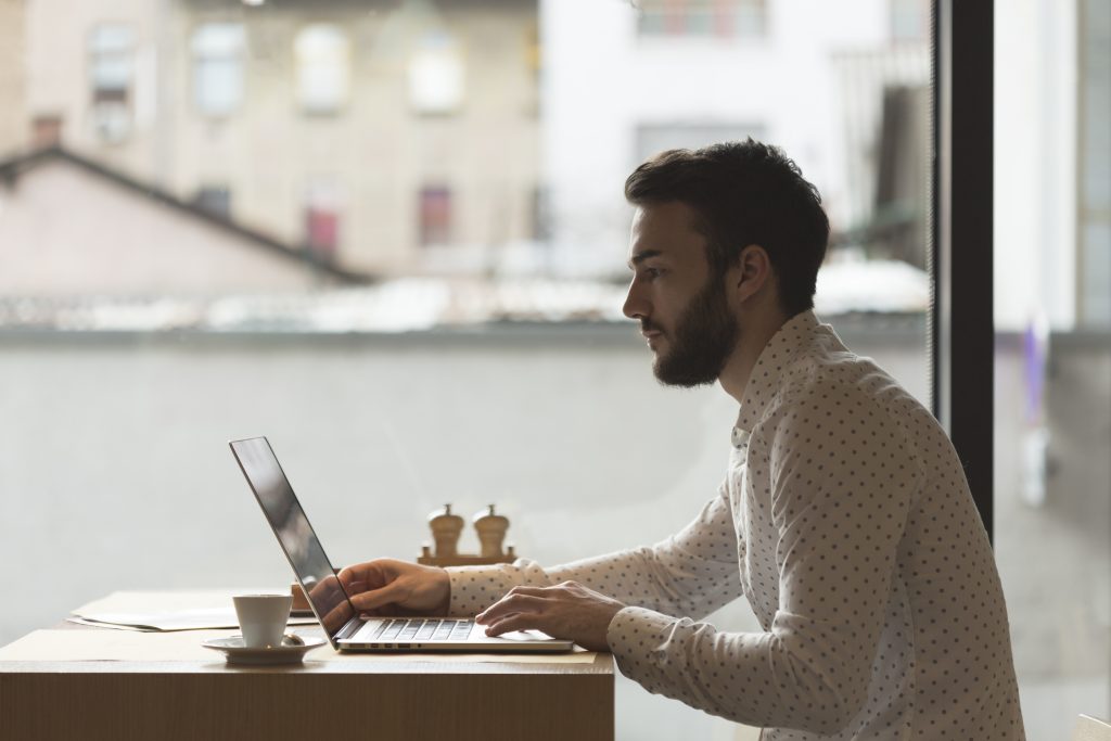 Bearded man intensely studying his laptop screen in a cafe.